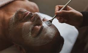 A person with closed eyes is lying down while a face mask is being applied to their face with a brush.