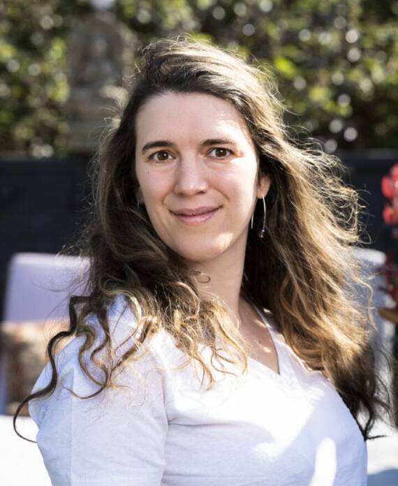 A professional spa therapist dressed in a white uniform standing in a serene treatment room, ready to provide expert wellness and massage services