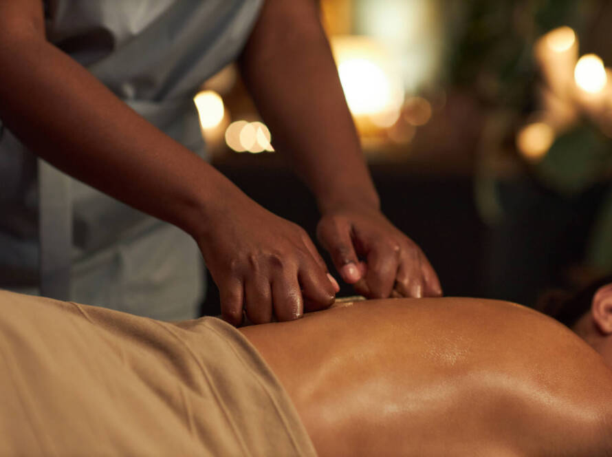 A person receives a back massage from a massage therapist in a softly lit room.