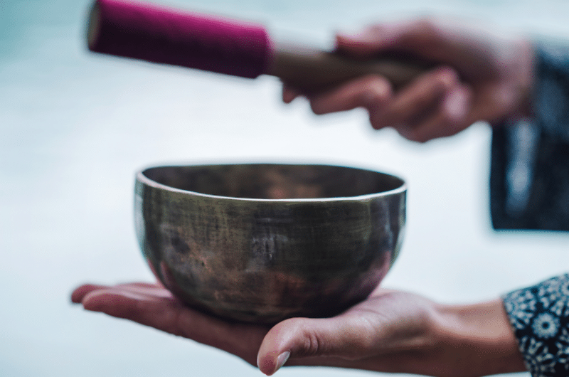A person holds a metal singing bowl in one hand and a mallet in the other, preparing to play the bowl.