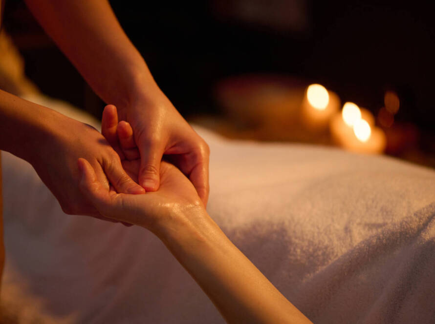 A person receives a hand massage on a white towel in a dimly lit room with candles in the background.