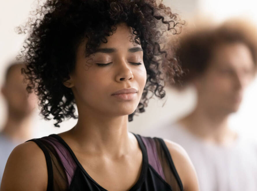 A person with curly hair and closed eyes appears to be meditating or focussing, with blurred individuals in the background.