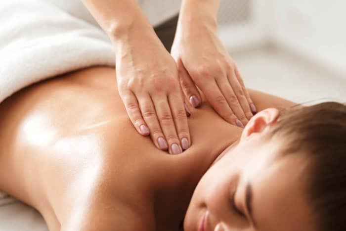 Person receiving a back massage whilst lying face down, with hands applying pressure to the upper back and shoulders.