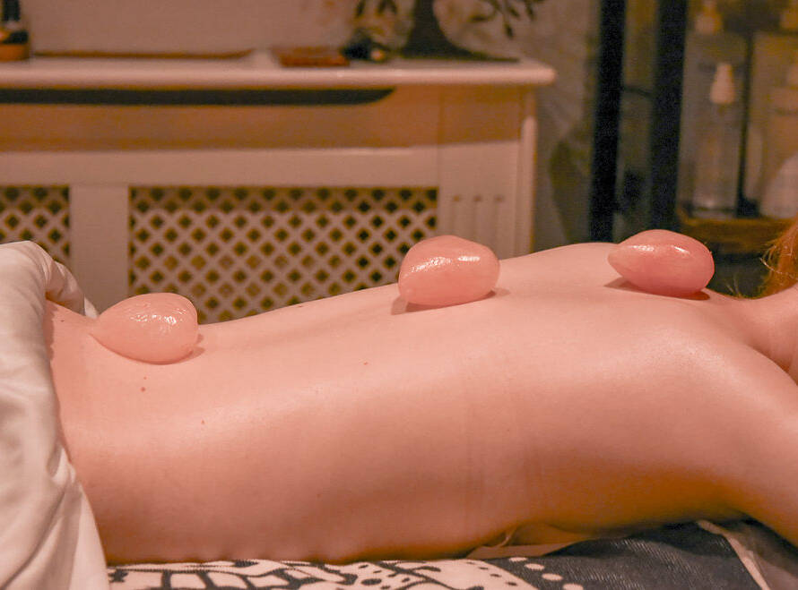 A person lies face down with three pink stones placed along their bare back, possibly during a spa or massage treatment.